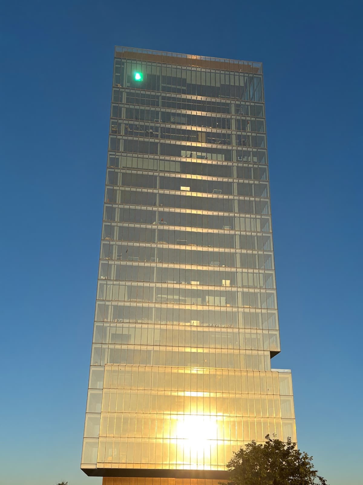Modern glass office tower reflecting warm golden sunset light against a clear blue sky